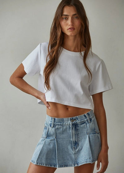 Woman wearing a white crop top and denim skirt against a plain background