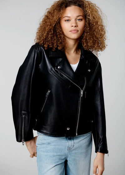 Person wearing a black leather jacket and light blue jeans on a plain background