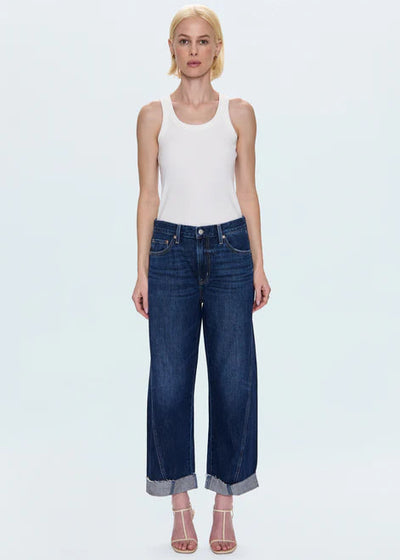 Woman wearing a white tank top and blue jeans on a light gray background
