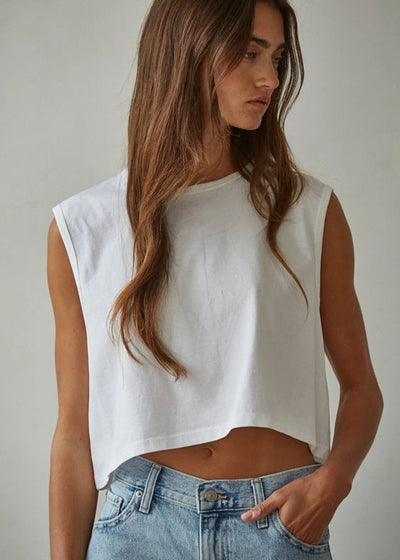 Woman wearing a white sleeveless top and blue jeans against a plain background