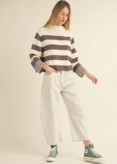 Woman wearing a striped sweater and white pants on a beige background